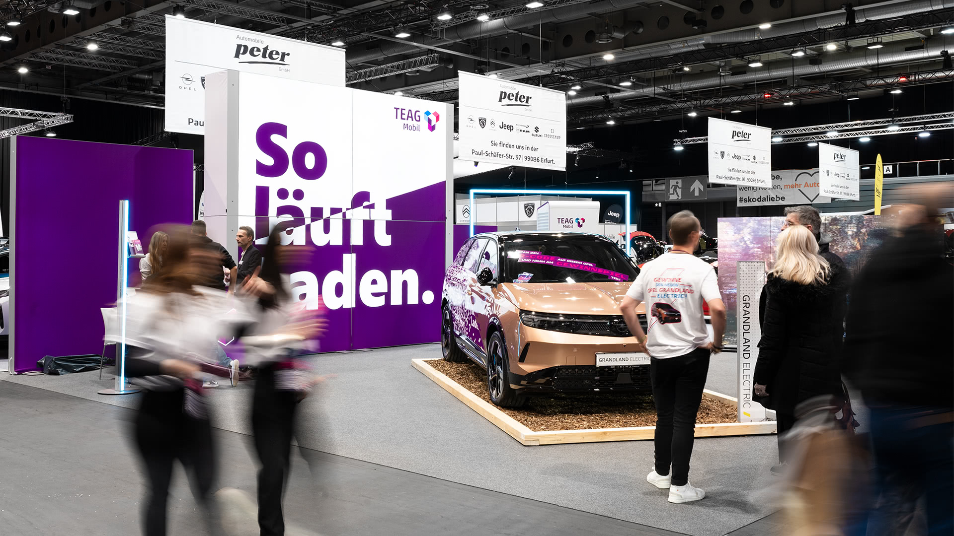 Ein glänzendes Elektroauto wird an einem modernen Messestand mit leuchtend lila-weißer Beschriftung ausgestellt.