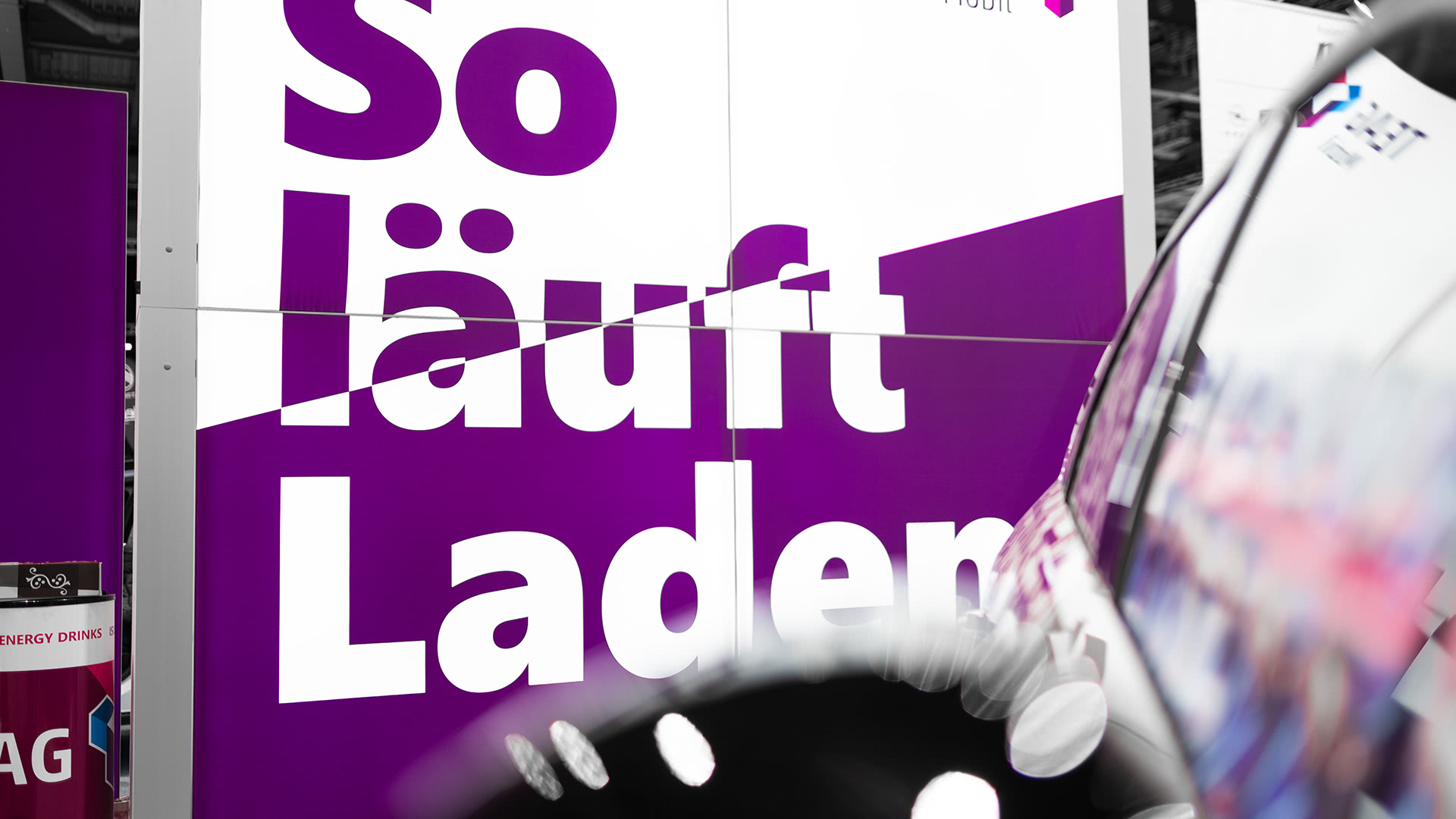 Großer deutscher Text So läuft Laden in fetten weißen Buchstaben auf einem lila-weißen Schild. Eine reflektierende Oberfläche, möglicherweise ein Auto, ist im Vordergrund auf der rechten Seite zu sehen.